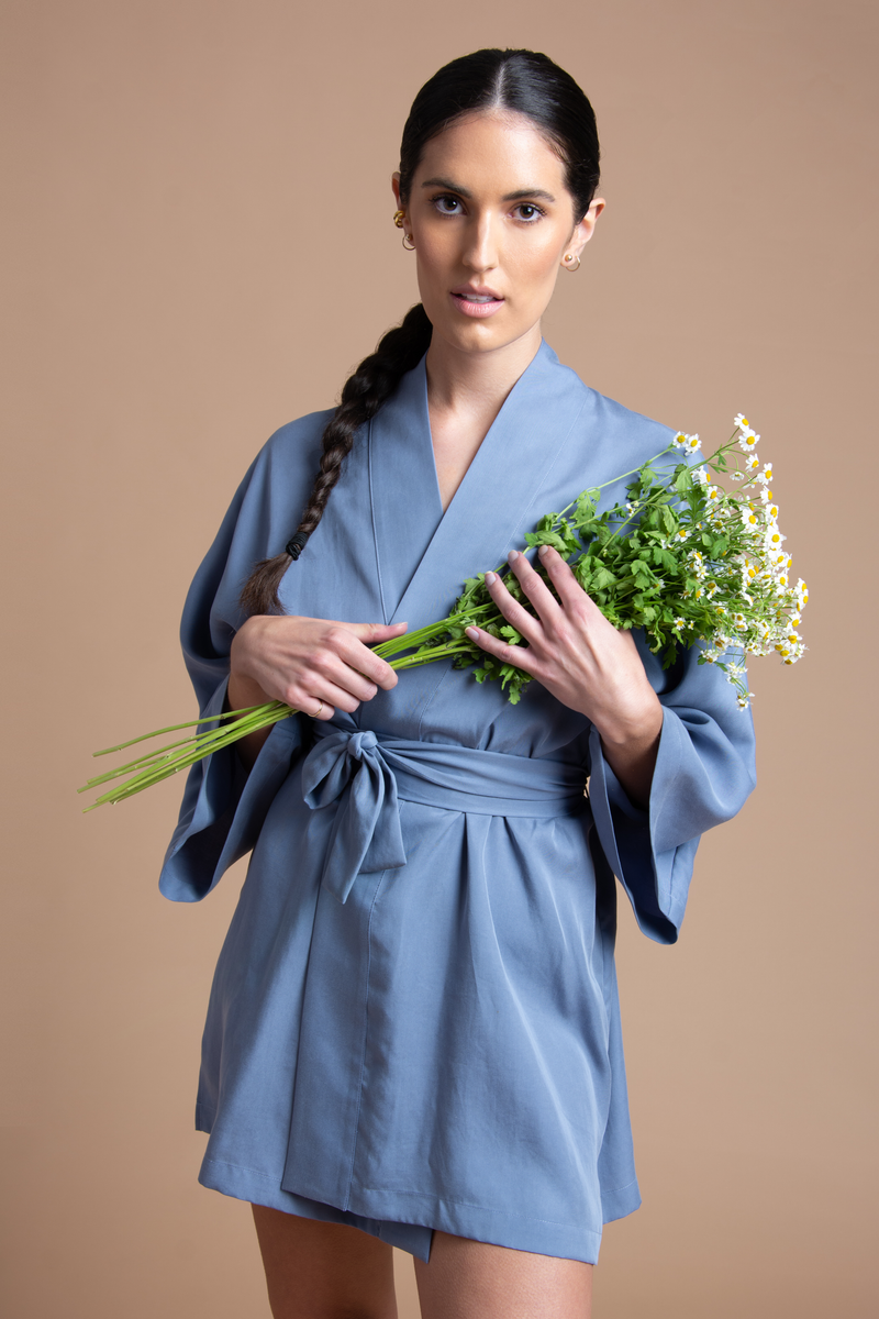 Model with a baby blue short kimono holding flowers and gazing at the camera.